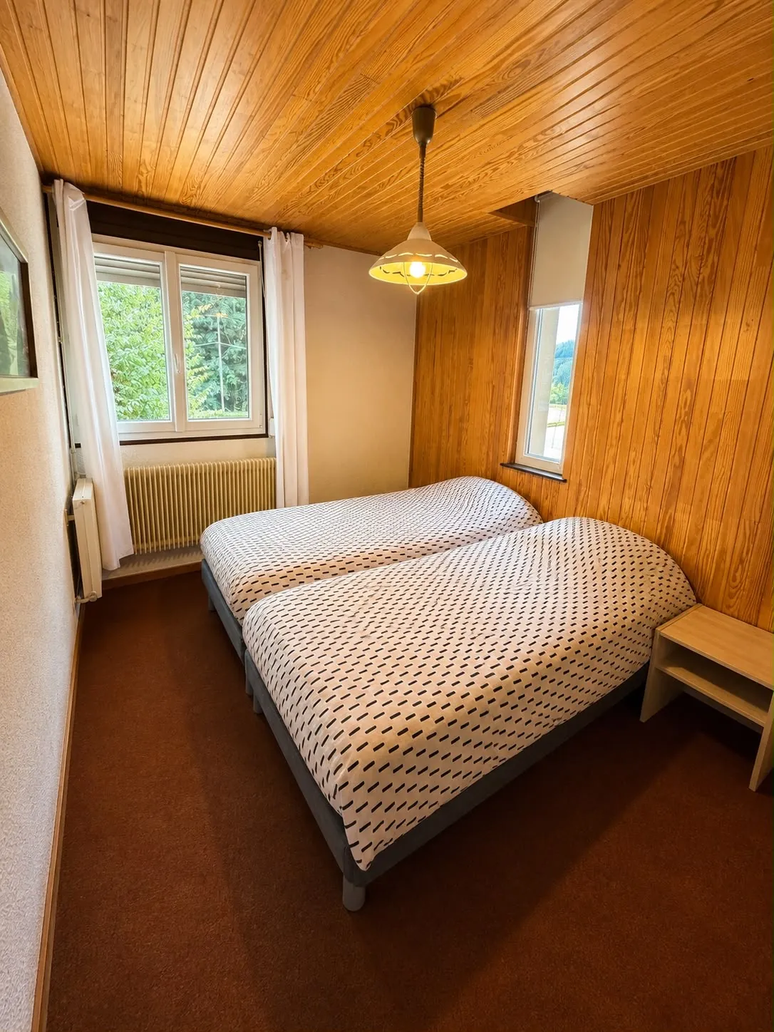 Chambre lambrissée avec deux lits jumeaux et vue sur la forêt
